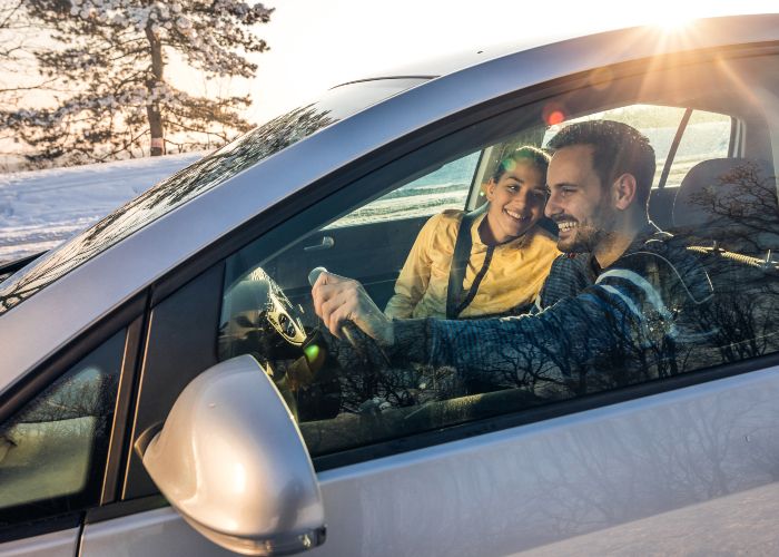 Couple souriant dans une voiture chaude et confortable en hiver.